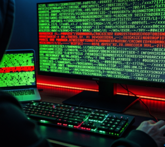 Hooded figure at a keyboard, monitor and laptop glowing with green terminal code, a line highlighted in red signifying an exploit