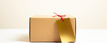 Plain cardboard box with an oversized blank gold price tag attached by a red string