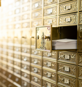 Wall of brass post office boxes with one door open showing envelopes