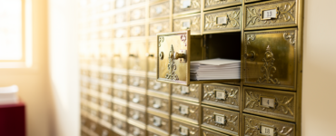 Wall of brass post office boxes with one door open showing envelopes