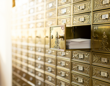 Wall of brass post office boxes with one door open showing envelopes