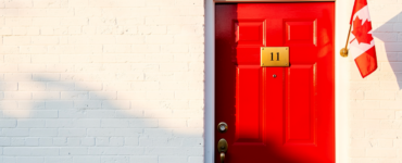 Bright red front door with brass number plate and a small Canadian flag