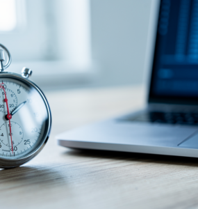 A stopwatch on a desk beside a laptop showing a terminal window