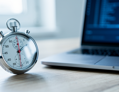 A stopwatch on a desk beside a laptop showing a terminal window